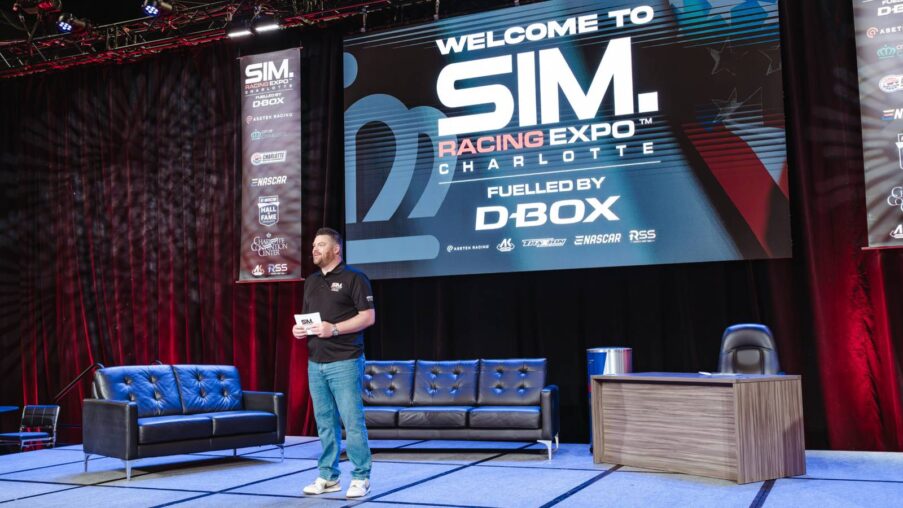 Wide interior view of the first US SimRacing Expo show floor with rows of racing simulator rigs, exhibitor booths, and attendees walking through the venue